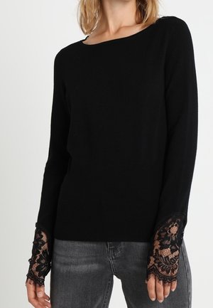 Black long-sleeve top with floral lace cuffs worn with faded black jeans, showing a casual yet elegant outfit.