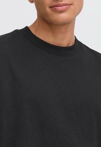 T-shirt en coton noir avec un col rond. Présentant des manches courtes et une texture douce et lisse. Design simple sans graphiques ni motifs.