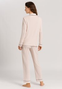 Lichtroze pyjama set bestaande uit een lange mouwen top met een kraag en zwarte biezen, gecombineerd met bijpassende relaxte broek. Zachte stof textuur.
