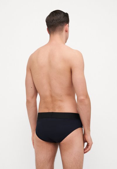 Schwarze Schwimmbriefs mit glatter Textur, ausgestattet mit einem breiten schwarzen Bund, passgenauer Form und minimaler Abdeckung, von hinten betrachtet.