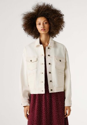 Veste en denim blanc à manches longues, fermeture par boutons, deux poches poitrine et des poches latérales. Portée sur une robe bordeaux à pois.