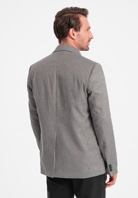 Grau karierter Blazer mit strukturierter Passform. Verfügt über einen Reverskragen, zwei Rückenschlitze und drei Knöpfe an den Ärmeln. Glatte Stofftextur.