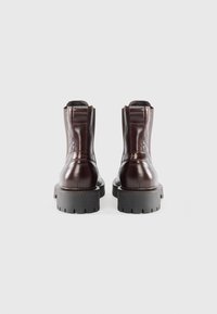 Bottines en cuir marron avec une finition brillante, une semelle en caoutchouc noir épaisse et deux panneaux élastiques sur les côtés pour un enfilage facile.