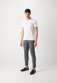 White T-shirt with "Marc O'Polo" logo, gray tailored pants, and black loafers. Model wears a black cap. Simple design, fitted silhouette.