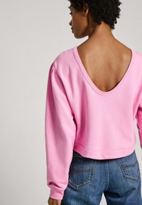 Rozā izgriezta sudraba džemperis ar dziļu V-veida aizmuguri un puffam garajām piedurknēm. Mīksta auduma, gluda tekstūra, apvienota ar zilu džinsu.