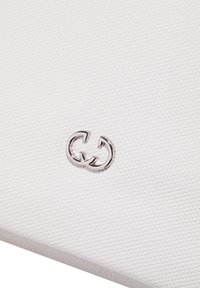 Matériau texturé blanc avec un accent de logo double-G argenté. La surface semble douce et structurée, soulignant un design minimaliste.