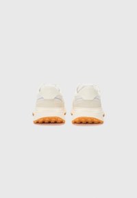 White and beige sneakers with a textured fabric upper and orange rubber sole, featuring subtle gray accents near the heel.