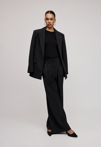 Sacou negru ajustat peste un top negru mulat, asociat cu pantaloni negri cu picioare largi și pantofi cu vârful ascuțit negri. Material neted, design structurat.