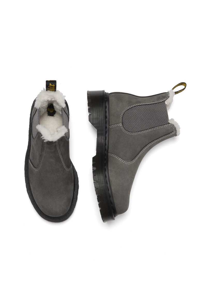 Grijze suede enkellaarsjes met wollen binnenlining, elastische zijkanten en een zwarte rubberen zool. Bovenaanzicht toont een ronde neus en contrasterende stiksels.