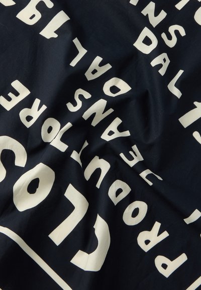 Σκούρο ύφασμα με λευκό, έντονο, κεφαλαίο κείμενο, μερικώς ορατό και παραμορφωμένο από τις πτυχές.