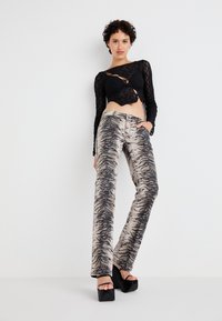 Musta, leikattu pitsi crop top, joka on yhdistetty korkeavyötäröisiin beigepantoihin, joissa on musta tiikeriraitakuosi ja levenevät lahkeet.