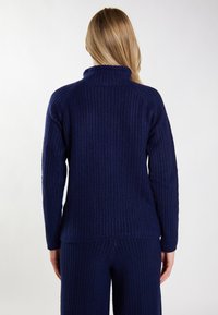 Granatowy sweter z prążkowanej dzianiny z wysokim kołnierzem, długimi rękawami i luźnym krojem. Teksturowany materiał dodaje głębi do projektu.