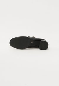 Scarpa nera con tacco alto, superiore in pelle liscia, suola in gomma texturizzata e decorazioni in metallo.