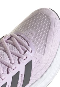 Chaussure de sport violet clair avec une tige texturée, un détail en lacets et un accent gris. Elle présente une semelle rembourrée et un matériau respirant.