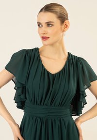 Smaragdgrünes Kleid aus fließendem Stoff, mit kurzen, gerüschten Ärmeln und einer taillierten Passform mit gerafften Details.