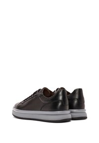 Zapatillas de cuero negro con una textura suave, suela de goma gris y cordones redondos. Presentan un diseño de caña baja y una estética minimalista.
