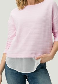 Haut rose pâle à manches longues avec une texture côtelée horizontale, ourlet blanc superposé et coupe décontractée. Assorti à un jean en denim bleu.