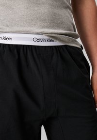 Zwarte sportbroek met een elastische tailleband en een wit Calvin Klein-logo. De stof lijkt zacht met een lichte glans.
