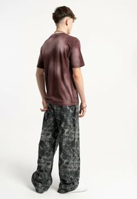 Bordowa koszulka z krótkim rękawem o efekcie gradientu, zestawiona z luźnymi spodniami w szarym kamuflażu, prezentującymi swobodną sylwetkę.