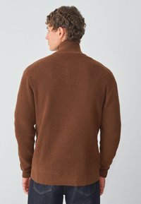 Suéter de punto acanalado marrón con cuello alto, mangas largas y dobladillo inferior ajustado, que presenta un acabado texturizado.