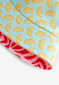Light blue fabric with yellow lemon slices pattern, featuring a red lining with pink tropical leaves design and quilted texture.