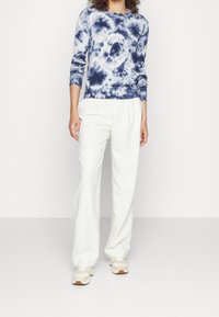 Mörkblå tie-dye sweatshirt med rund halsringning, ribbade muddar och fåll, kombinerad med off-white vida byxor och ljusa sneakers.