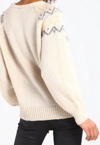 Krämbelagd stickad tröja med en avslappnad passform, prydd med ett texturerat mönster i grått vid axelsömmarna samt ribbad mudd och nederkant.