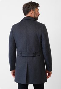 Grå uldfrakke med rygklap, spidse lapels og dobbeltknapbælte detaljer. Har skræddersyet pasform og glat tekstur.