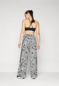 Μαύρο αθλητικό σουτιέν με διασταυρούμενες τιράντες συνδυασμένο με φαρδιά παντελόνια μαύρου και λευκού χρώματος που διαθέτουν τροπικά μοτίβα και γεωμετρικά σχέδια.