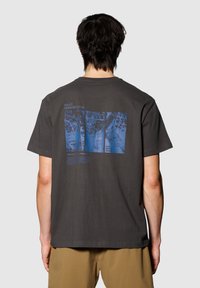 Szara bawełniana koszulka z luźnym krojem, z niebieską grafiką i tekstem na plecach, przedstawiająca mapy miast i typografię.