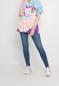 Camiseta de tie-dye colorido con patrones de remolinos en azul, naranja y púrpura, combinada con jeans ajustados azules y zapatillas gris y blancas.