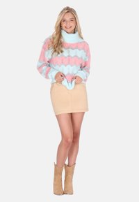 gebreide trui met een roze en blauwe zigzagpatroon; hoge kraag; gecombineerd met een beige minirok en tan cowboylaarzen.