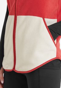 Red and cream fleece vest with zip closure, featuring side pockets and contrasting black sleeves. Soft texture with a color-block design.