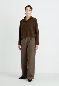 Brown pullover with a collar, long sleeves, and a relaxed fit, paired with high-waisted, wide-leg, dark brown pants and black flats.