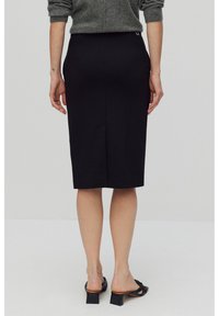 Svart pennkjol med en elegant design, bakslits för ökad rörelsefrihet, ihop med svarta blockklackade sandaler.