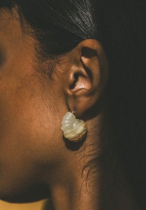 Gros plan sur l'oreille d'une personne aux cheveux foncés portant une boucle d'oreille en pierre texturée de couleur claire, unique.