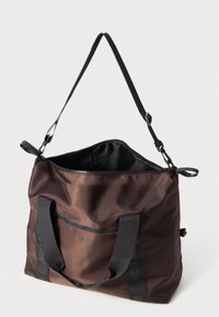 Καφετί νάιλον τσάντα tote με φερμουάρ στην κορυφή, αντίθετους σκούρους ιμάντες και μπροστινή τσέπη. Λείες υφές με ελάχιστες λεπτομέρειες σε υλικά.