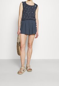 Navy sleeveless top with floral print, paired with dark shorts. Accessorized with a woven bag and beige sandals.