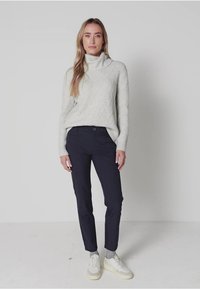 Lichtgrijze gebreide turtlenecktrui met een textuurpatroon, gecombineerd met marineblauwe pantalon en witte sneakers. Eenvoudig, hedendaags ontwerp.
