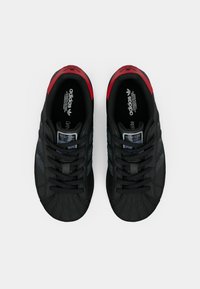 Μαύρα αθλητικά παπούτσια με υφή, με κόκκινες λεπτομέρειες, μύτη σε σχήμα κέλυφους και μαύρα κορδόνια. Περιλαμβάνει πολύχρωμη λεπτομέρεια λογότυπου.