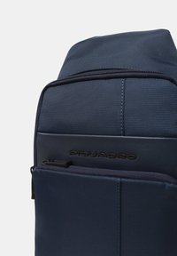 Zaino Piquadro blu navy in tessuto strutturato, con tasca frontale con cerniera e pannello similpelle con nome del marchio in rilievo.