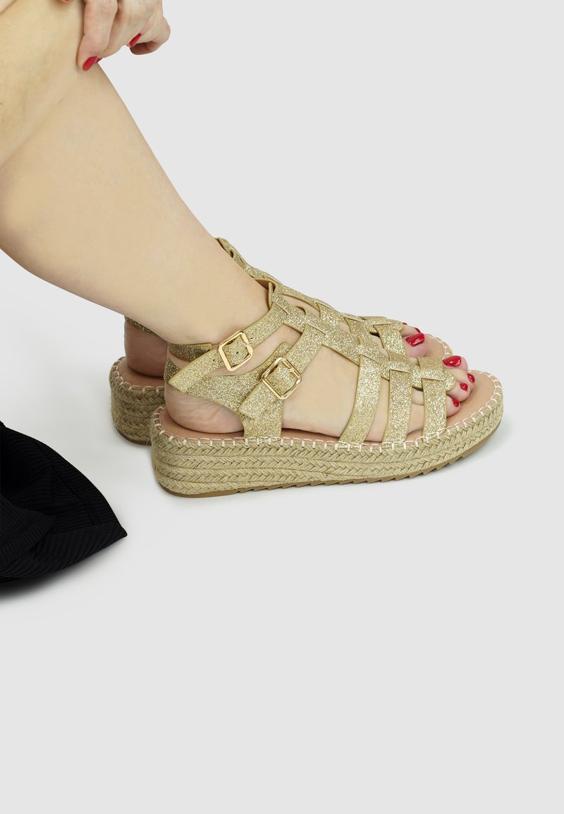 Gold glitter platform sandals with multiple cross straps, adjustable buckles, and woven jute soles. Flat, textured outsole visible.