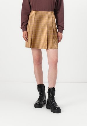 Brown long-sleeve shirt paired with a pleated yellow checked skirt and black lace-up ankle boots with thick soles. Patterned textile detail visible.