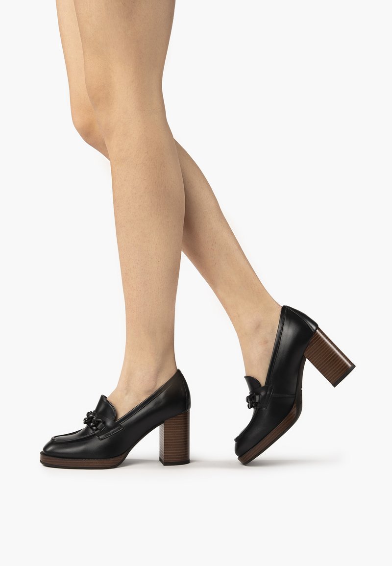 Chaussures à plateforme en cuir noir avec un bout rond, un détail en nœud et un talon en bois empilé. Texture lisse et design structuré.