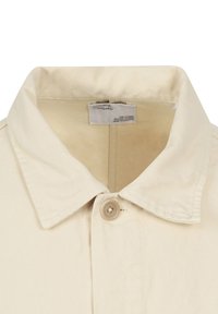 Giacca beige chiaro con colletto classico, chiusura a un bottone e tessuto strutturato. Etichetta di cura visibile all'interno del colletto.