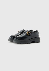 Black leather loafers with thick rubber soles and gold buckle details on a plain light background.