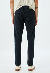 Vaqueros de mezclilla azul oscuro con un corte recto, que cuentan con bolsillos traseros y una etiqueta de cinturilla texturizada, combinados con zapatos deportivos blancos.