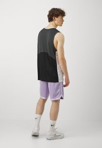 Sort og grå ærmeløs sportstop med kontrasterende lyserøde sidepaneler, parret med lyse lilla shorts og hvide træningssko.