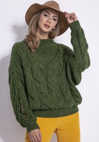 Zielony, oversize sweter z grubym splotem, z prążkowanymi mankietami i dołem; z rozcięciami na ramionach. Połączony z żółtymi spodniami z kordurowej tkaniny.