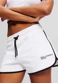 Baltos šortai su juodu apvadu ir raišteliu. Yra "Karl Lagerfeld Jeans" logotipas ant apatinės dalies. Pagaminti iš minkštos medžiagos.